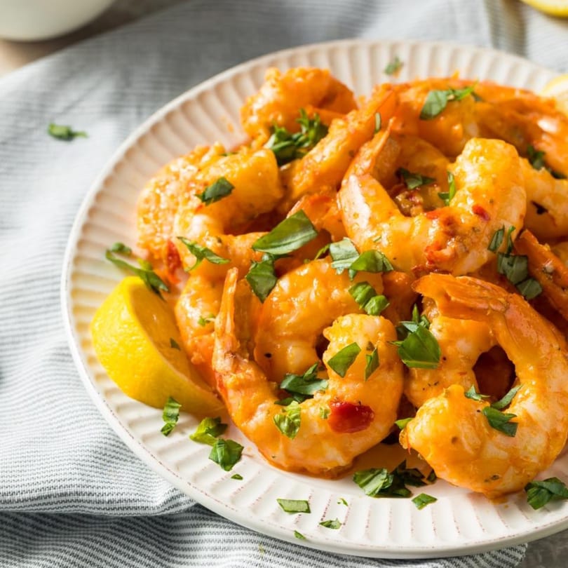 Dominican-style shrimp in a creamy orange sauce, garnished with fresh herbs and a lemon wedge.