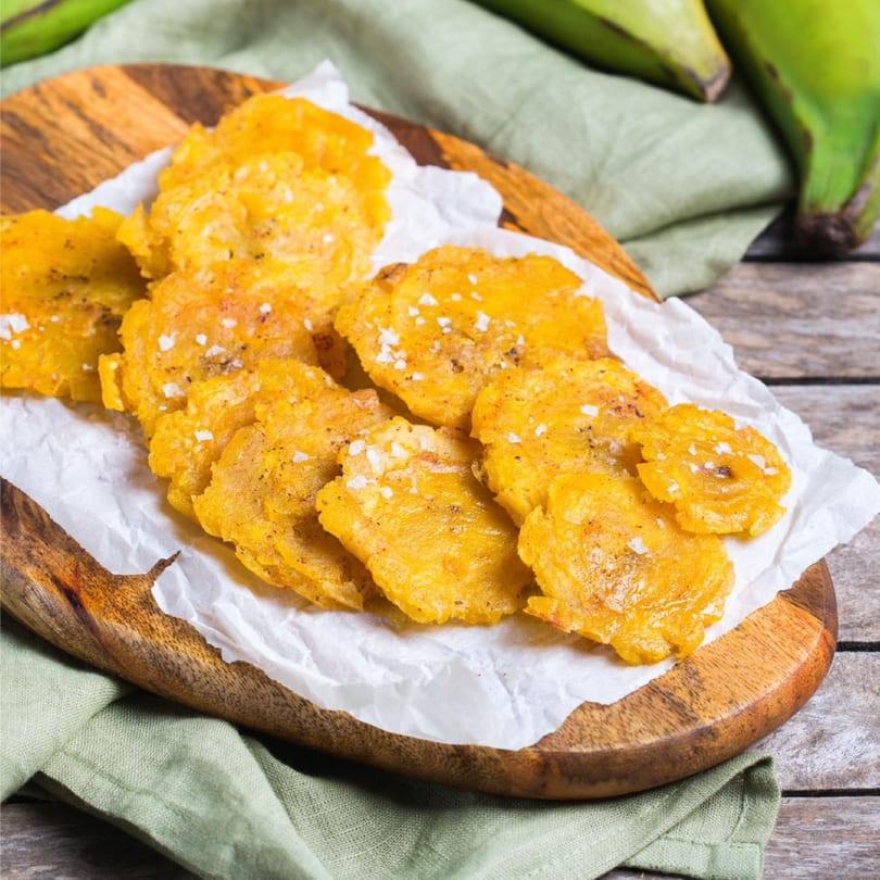 Golden tostones, or fried plantains, sprinkled with salt and pepper on a wooden board.