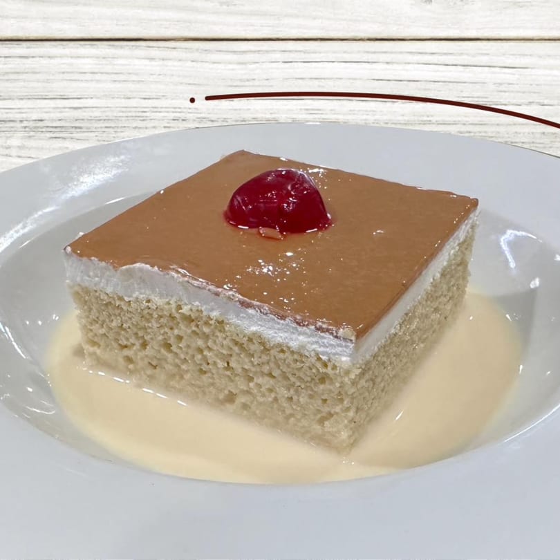 A slice of Dominican tres leches cake with a cherry on top, served in a white bowl.