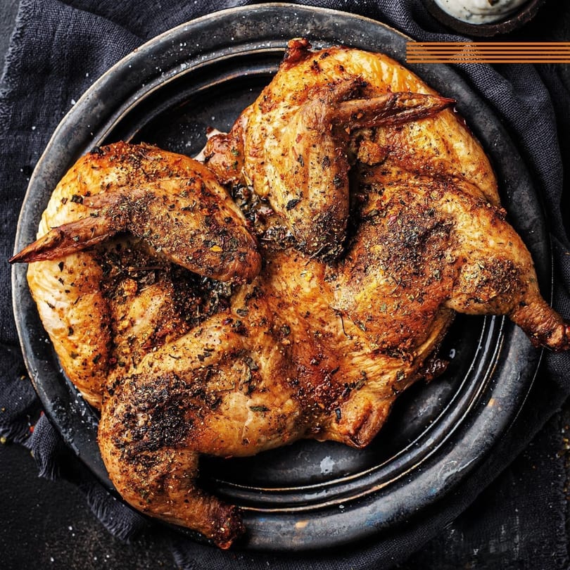 Whole roasted chicken, seasoned with herbs and spices, served on a dark plate.
