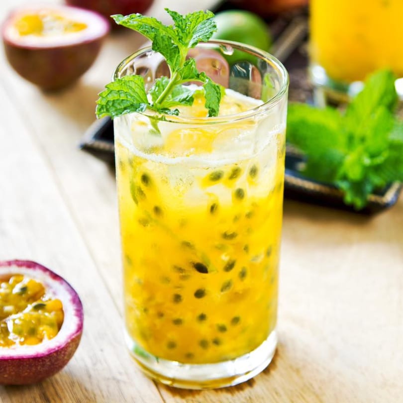 A refreshing passion fruit drink with ice and mint, next to a halved passion fruit.