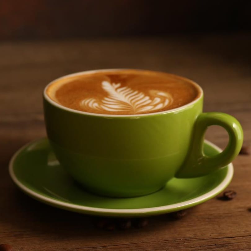 A vibrant green cup of latte with intricate leaf-shaped latte art sits on a wooden table.