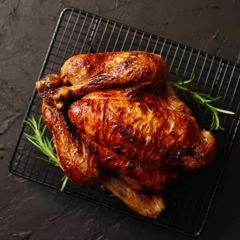 Whole roasted chicken with crispy skin and rosemary sprigs on a black cooling rack.