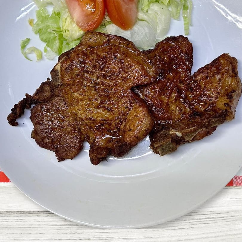 Two golden-brown fried pork chops with a side of lettuce and tomato on a white plate.