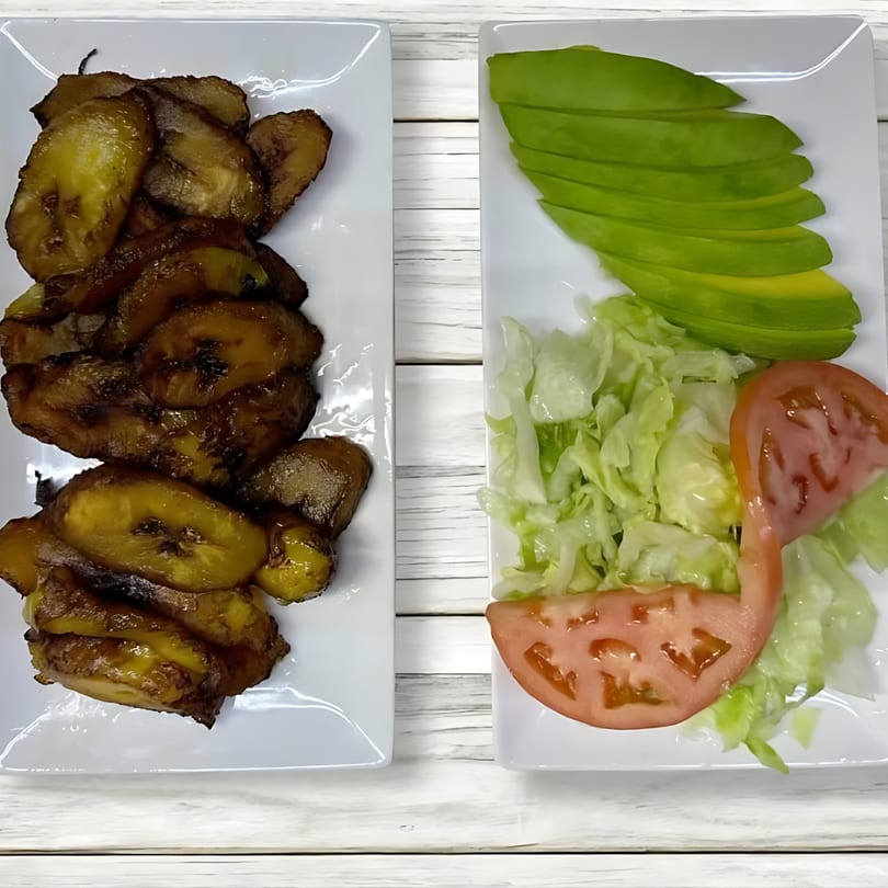 Two plates of Dominican food: fried plantains on the left, and a salad with avocado, lettuce, and tomato on the right.