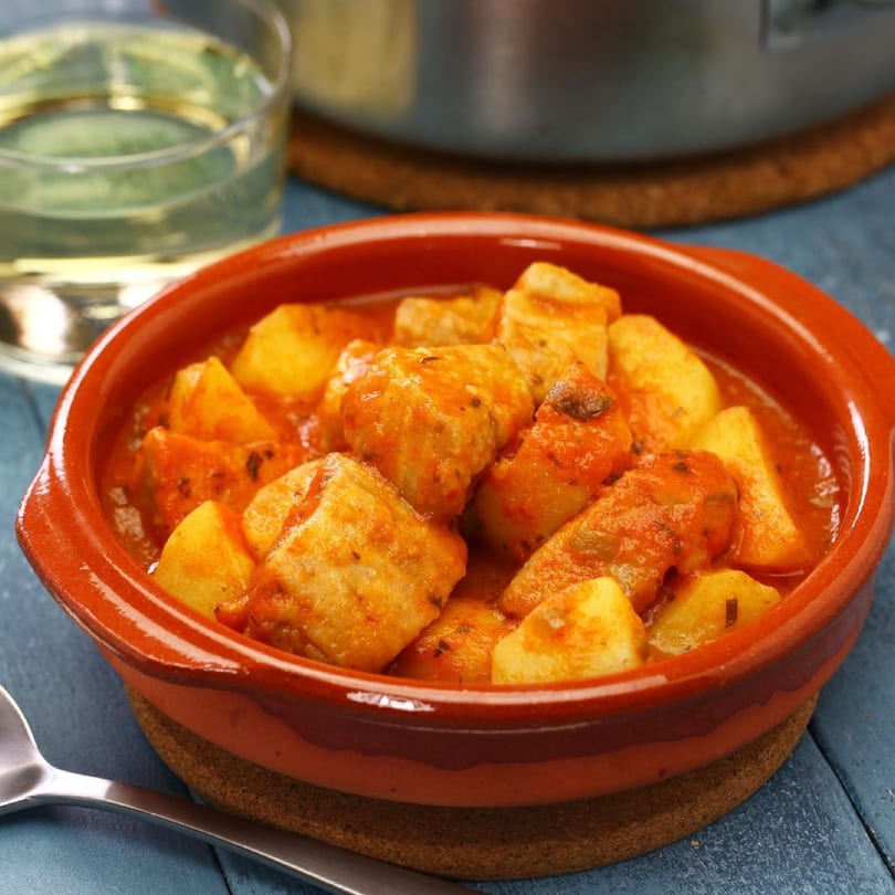 Dominican stew with chunks of meat and potatoes in a rich red sauce, served in a rustic terracotta bowl.